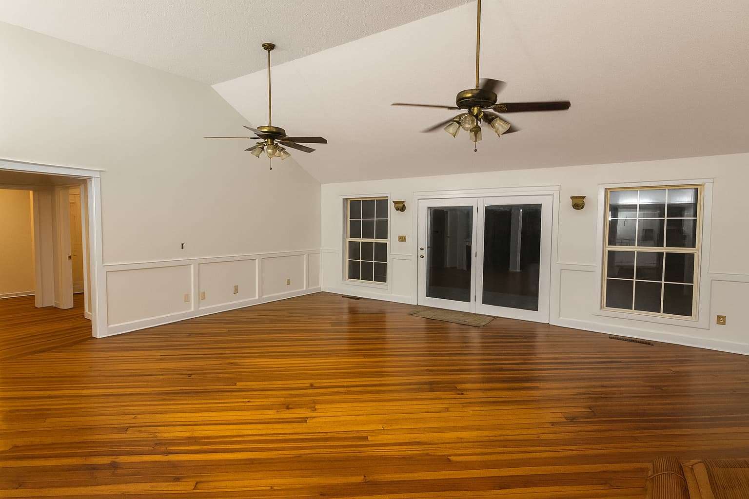 Spacious interior of a house behind front double doors with wooden floors and two chandeliers with ceiling fans